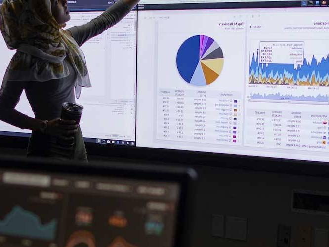 Woman is standing infront of a projector pointing to graphs on the screen